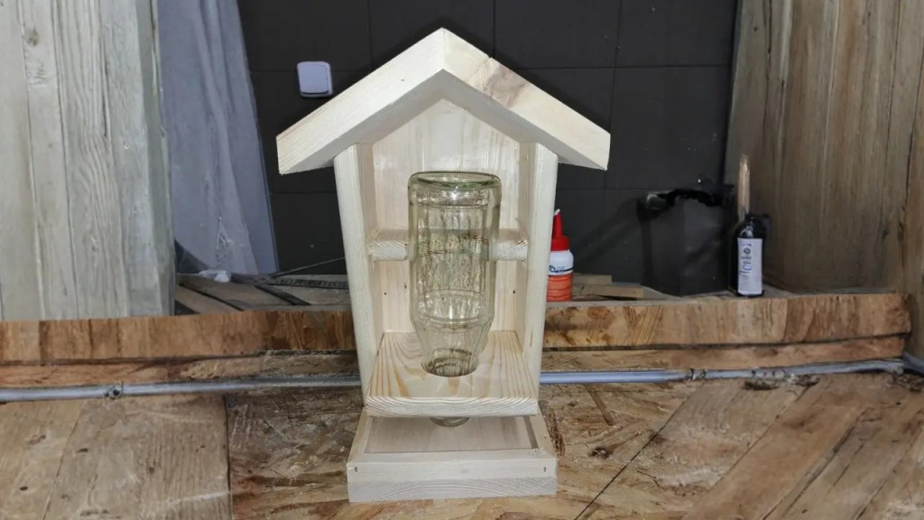 Vogelfutterhaus mit Glasflasche als Futtersilo in der Werkstatt auf rustikalem Holz präsentiert. 