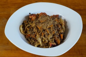 Linsenpfanne in einem Suppenteller auf rustikalem Holzbrett