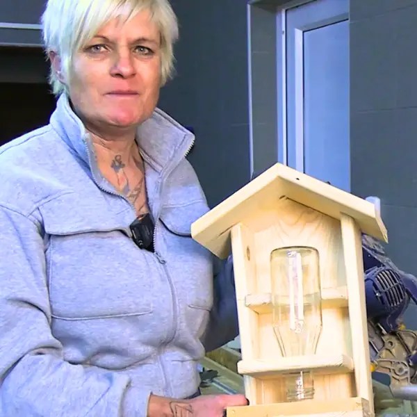 Person in Werkstatt zeigt selbst gebautes Vogelfutterhaus mit Glasflasche als Futtercontainer