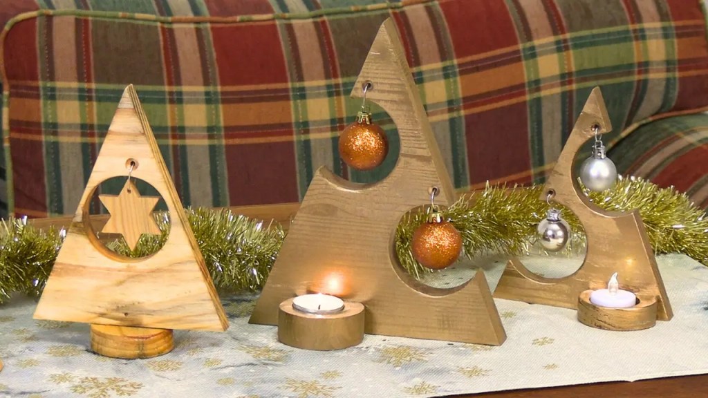 3 Holzweihnachtsbäume aus einem Fichtenbrett mit Kugeln und Sternen. Der Ständer mit einer Vertiefung als Kerzenständer auf einer weihnachtlichen Tischdecke mit einem rustikalen Sofa im Hintergrund.